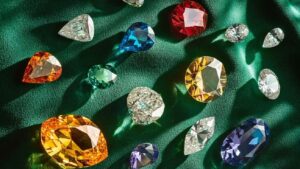 A top-down view of various colorful diamonds scattered across a square emerald-green velvet surface (1)